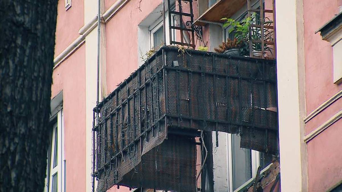 Drewniany balkon z metalową kratownicą, pokryty materiałem ochronnym, na różowej fasadzie budynku.