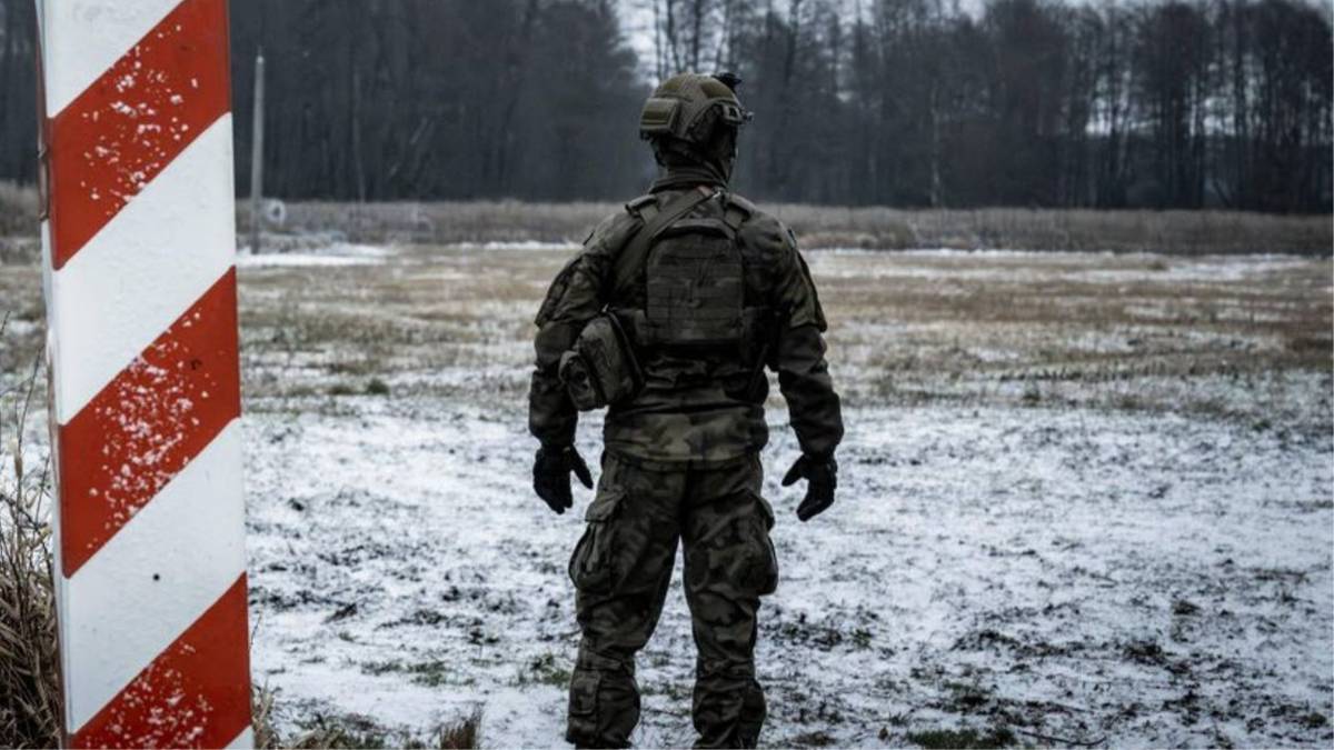 Żołnierz w umundurowaniu stoi na tle zaśnieżonego terenu obok słupka granicznego.