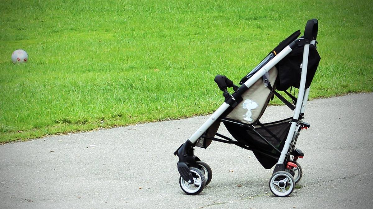 Pusty w&oacute;zek dziecięcy na chodniku z zieloną trawą w tle.