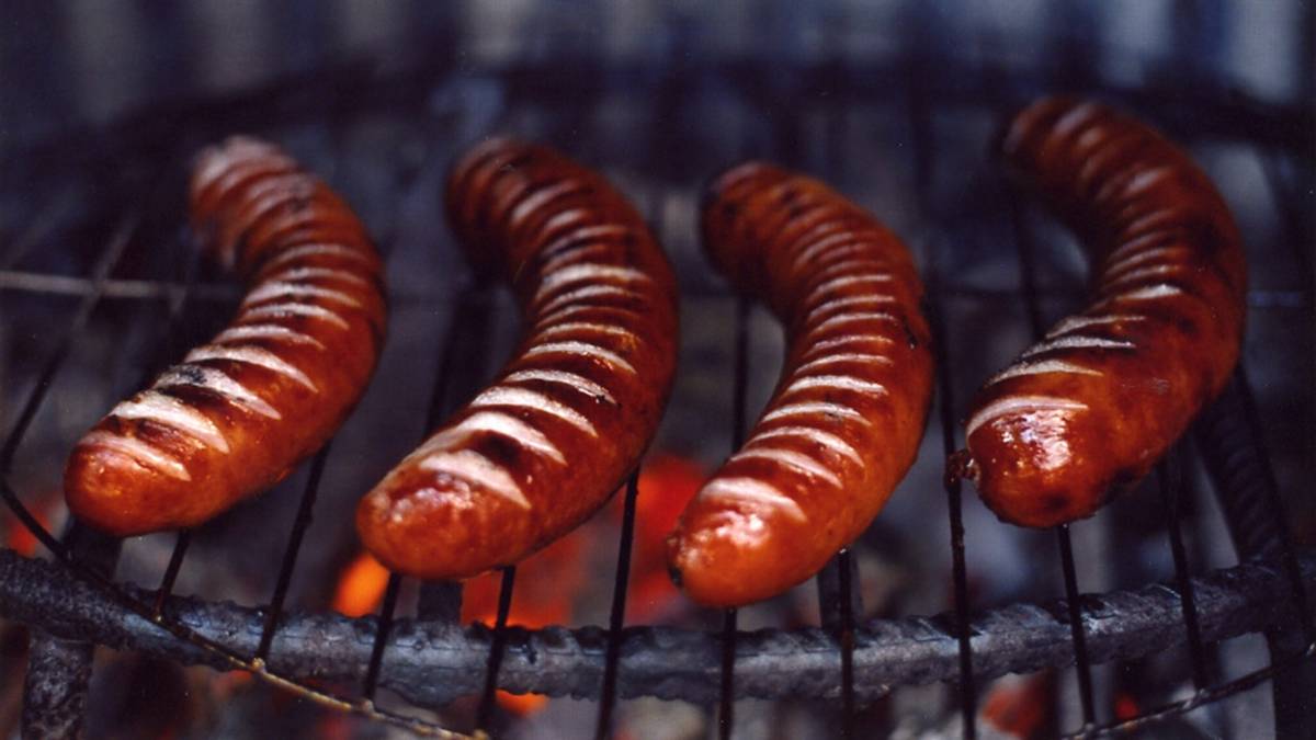 Cztery kiełbaski smażone na ruszcie nad żarem.
