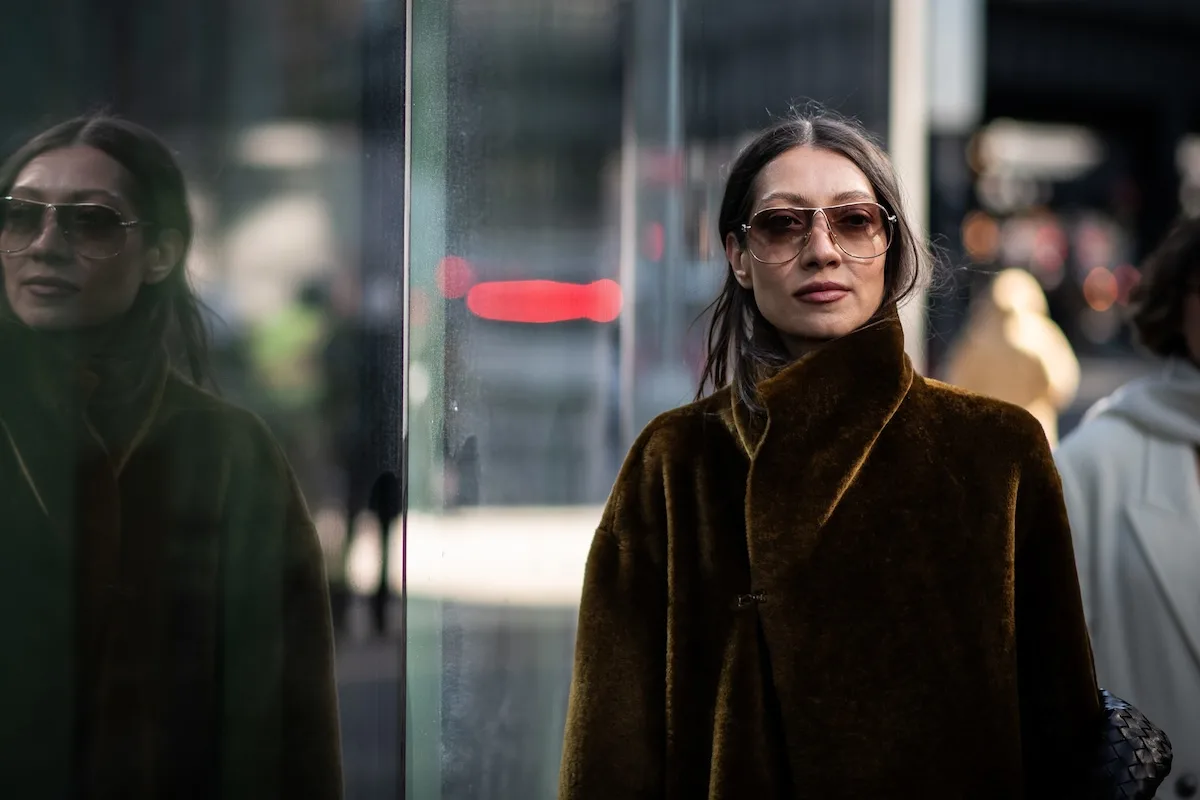 Kobieta w minimalistycznym, luksusowym płaszczu stoi przy przeszklonej witrynie, prezentując nowoczesny styl miejski. Zakupy takich ubrań z zagranicznych platform mogą się zmienić, ponieważ Unia Europejska planuje wprowadzenie opłaty manipulacyjnej dla przesyłek spoza UE.