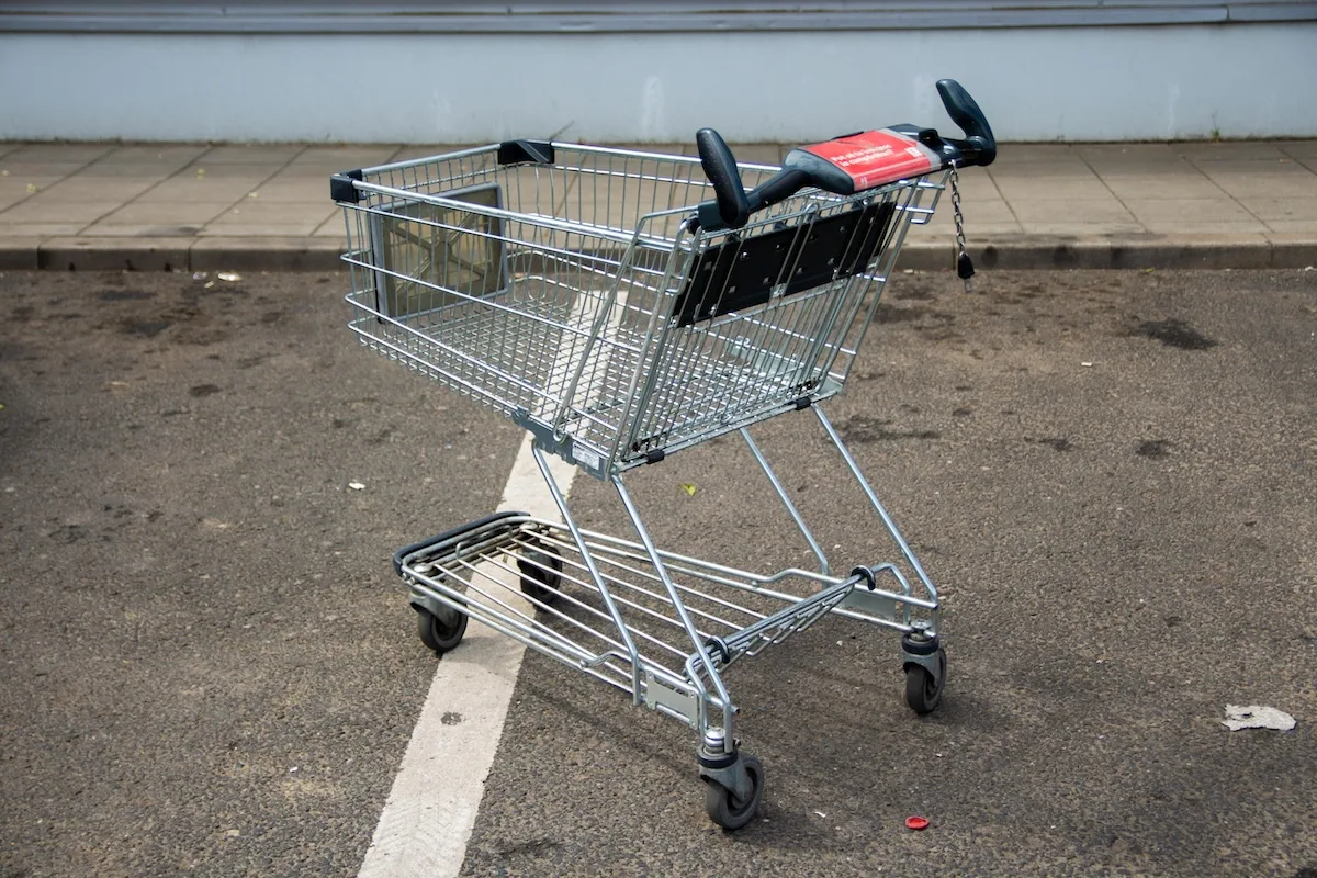 Porzucony wózek zakupowy na parkingu – symbol kryzysu w sprzedaży detalicznej i bankructwa sieci marketów dyskontowych.