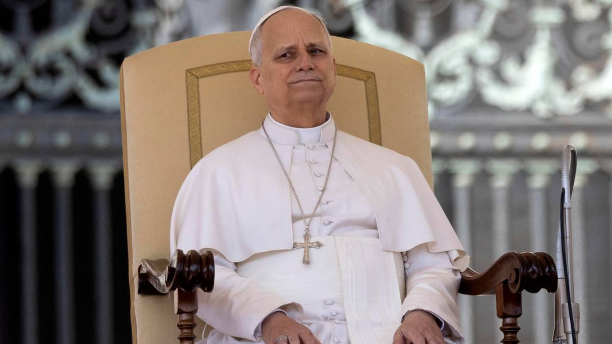 Papież Leon XIV w białej szacie papieskiej siedzi na ozdobnym krześle.