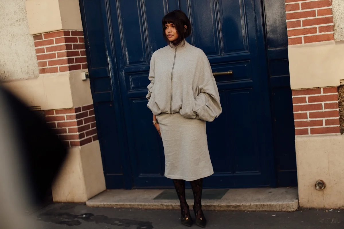 Modelka w minimalistycznej, szarej stylizacji H&amp;M – oversize’owa bluza i spódnica midi – stoi przed granatowymi drzwiami kamienicy.