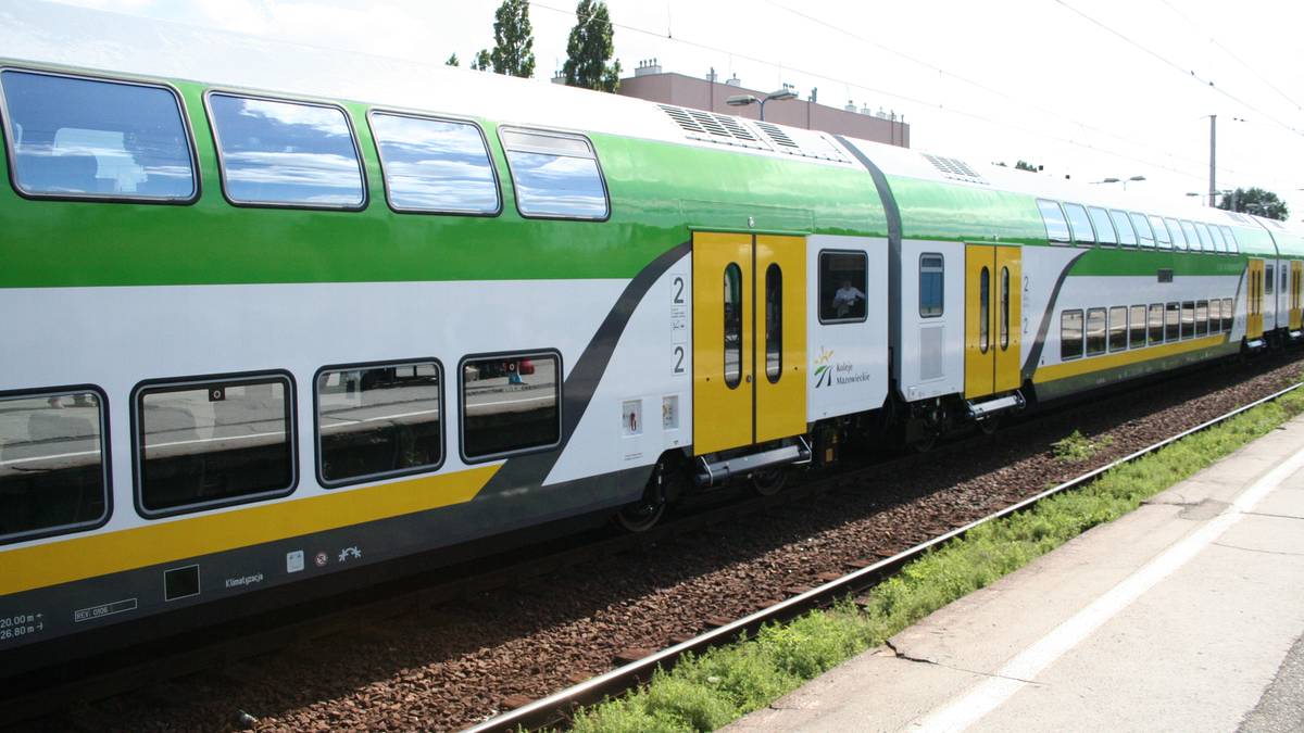 Dwupiętrowy pociąg Kolei Mazowieckich w kolorach zielonym, białym i ż&oacute;łtym na torach kolejowych.