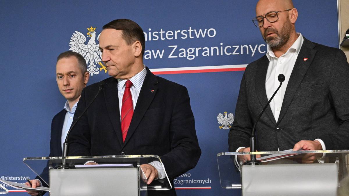 Trzech mężczyzn stoi przy mównicach na tle niebieskiej ściany z logo Ministerstwa Spraw Zagranicznych.