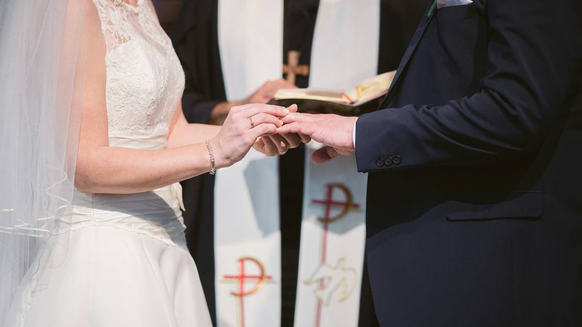 Zbliżenie na dłonie pary młodej podczas wymiany obrączek podczas ceremonii ślubnej w kościele, z widocznym fragmentem szaty duchownego.