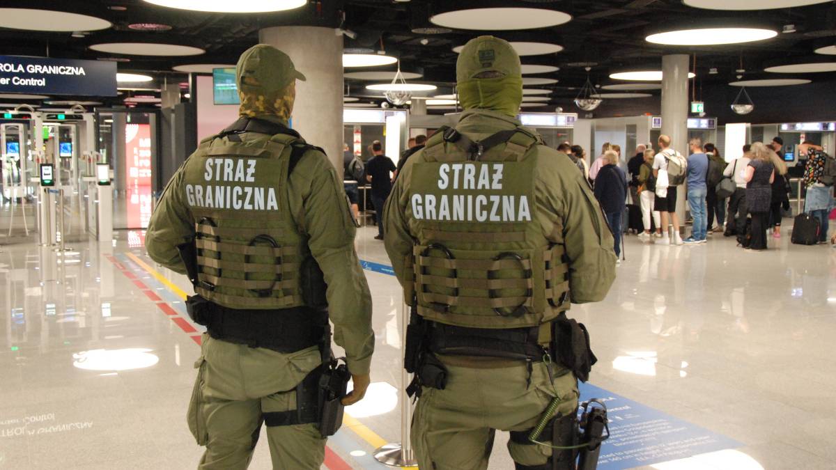 Dwóch funkcjonariuszy Straży Granicznej w mundurach patrzy w stronę terminala lotniska.
