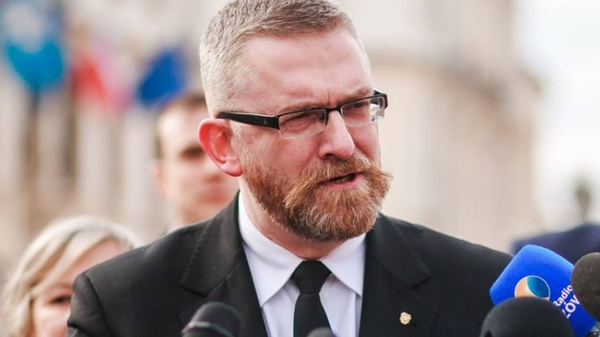 Mężczyzna w garniturze z okularami i brodą, mówiący do mikrofonu.