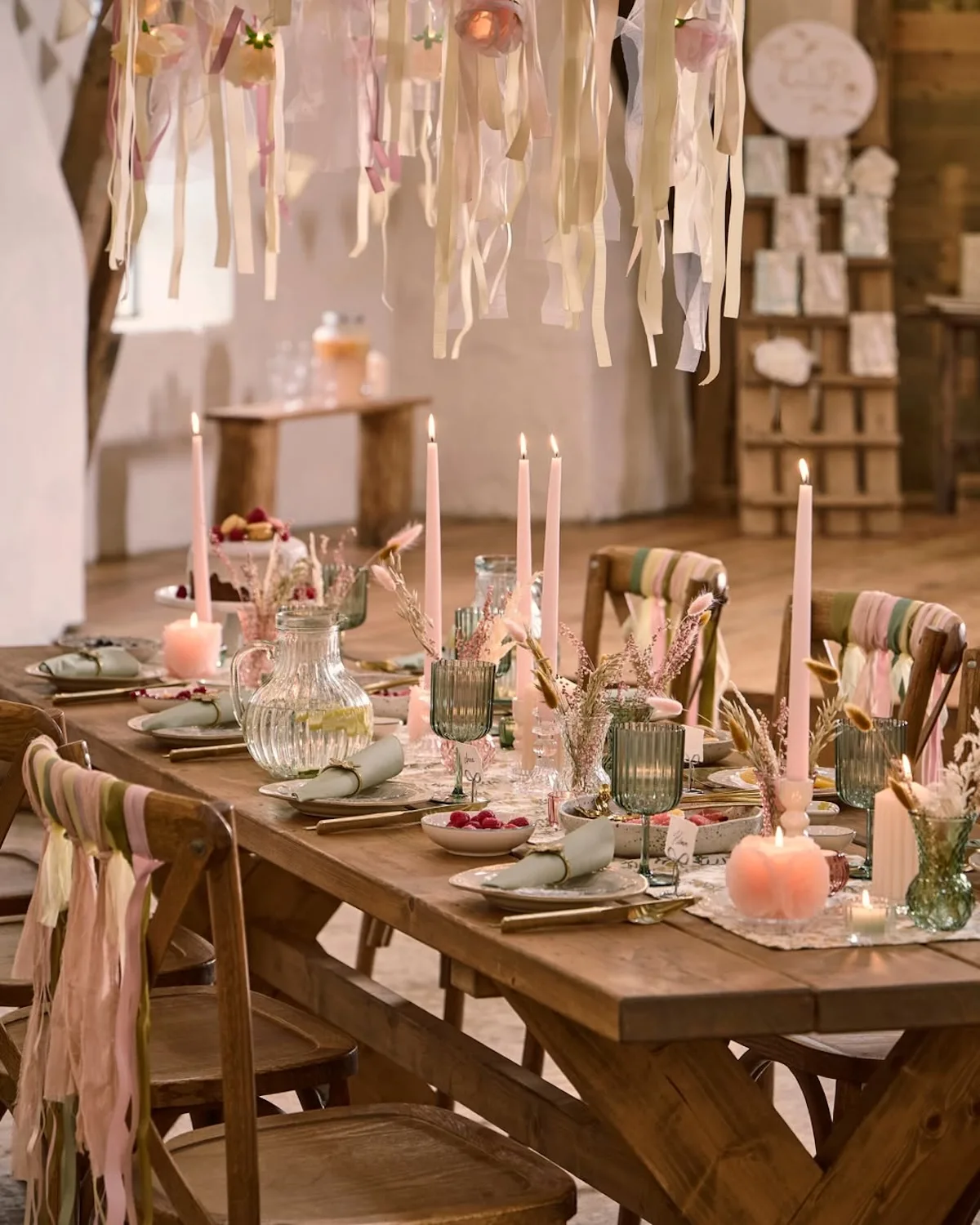 Pastelowa aranżacja stołu w stylu skandynawskim – drewniany stół z dekoracjami, świecami, szkłem i tekstylnymi ozdobami w odcieniach różu i beżu.