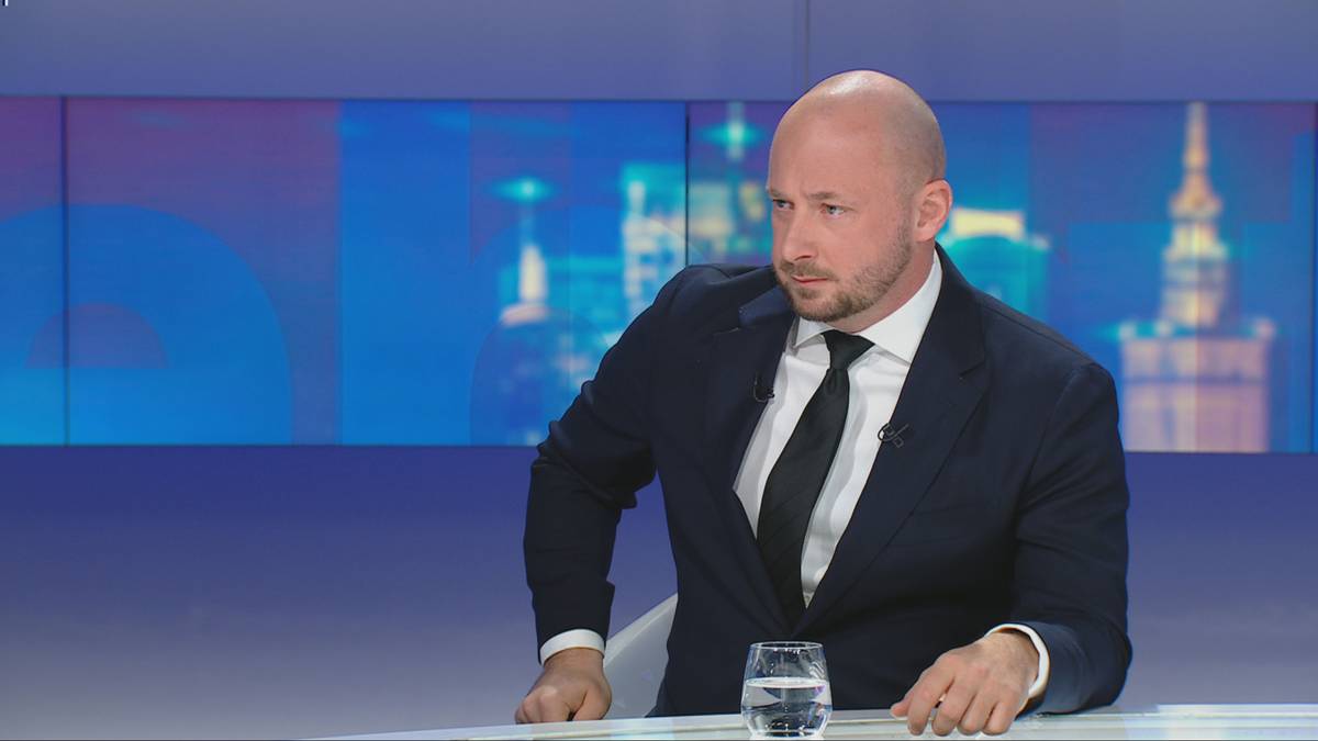 Mężczyzna w garniturze siedzi przy stole, patrząc w bok.