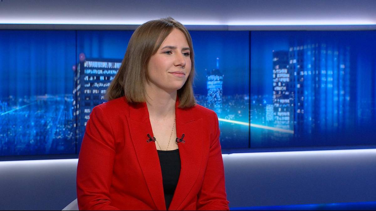 Kobieta w czerwonym żakiecie siedzi w studiu telewizyjnym.