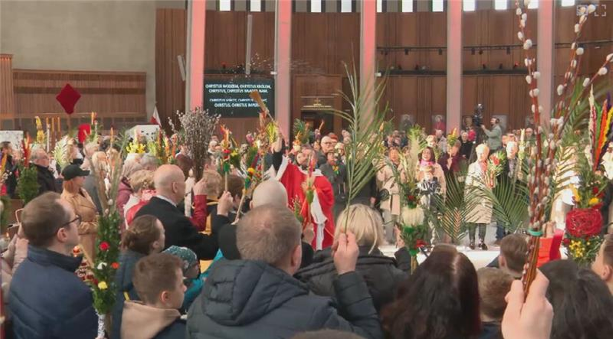 Grupa wiernych w kościele trzymająca palmy i gałązki podczas uroczystości Niedzieli Palmowej.
