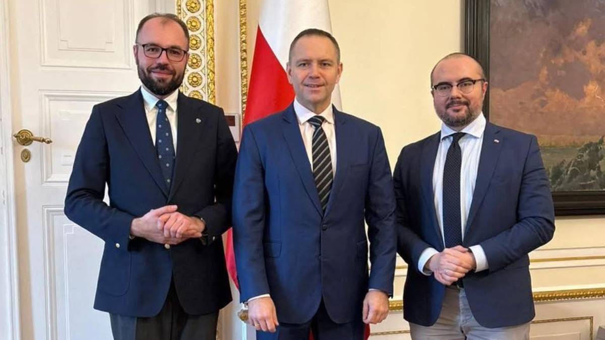 Trzech mężczyzn w ciemnych garniturach stoi obok siebie, pozując do zdjęcia.