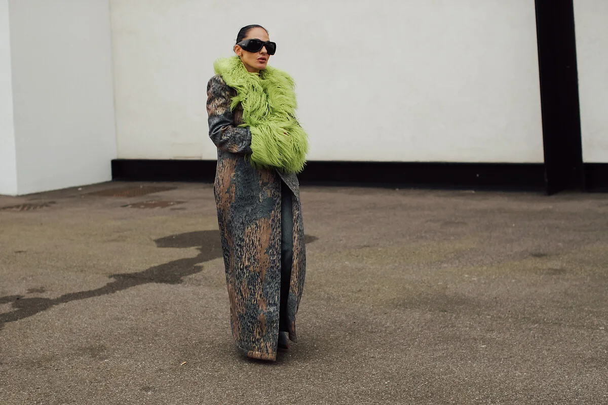 Modivo przejmie Moliera2? Kobieta w długim płaszczu z zielonym futrzanym kołnierzem i dużych czarnych okularach przeciwsłonecznych podczas tygodnia mody w Mediolanie.