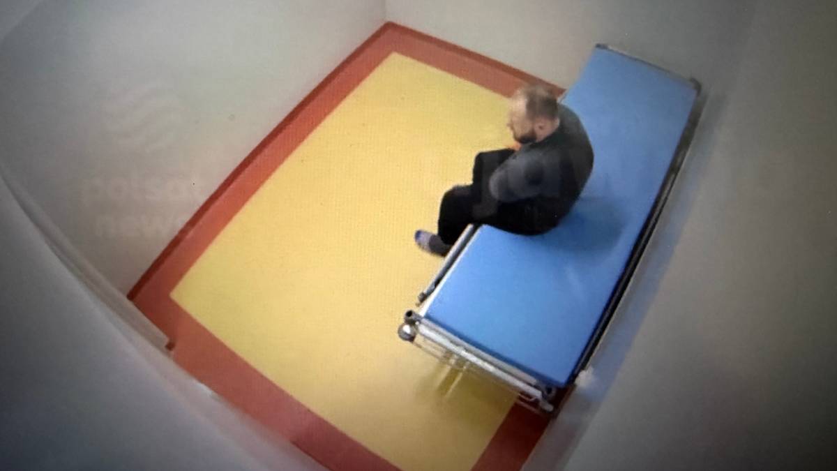 Mężczyzna siedzi na łóżku w pustym pokoju.