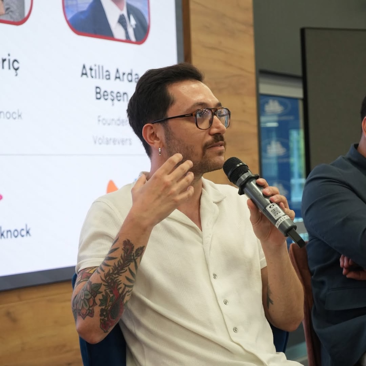 Bliski kadr na prelegenta ze startupu Replenit – mężczyzna w jasnej koszuli i okularach mówi do mikrofonu podczas panelu.