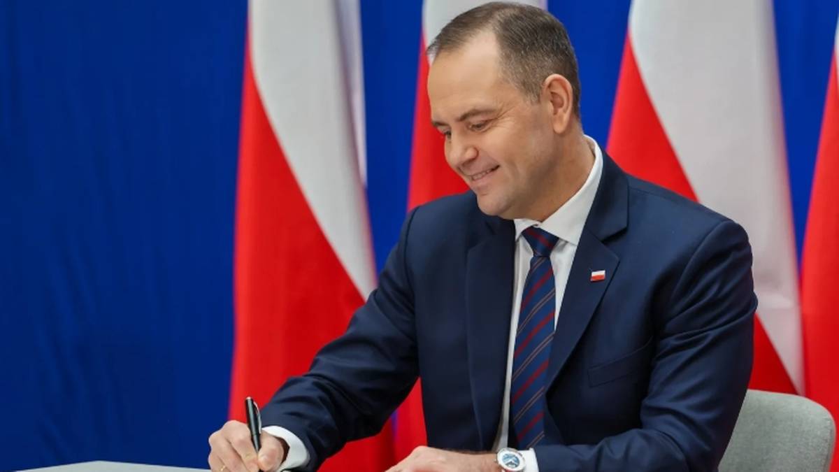 Mężczyzna w garniturze podpisuje dokument na tle flag