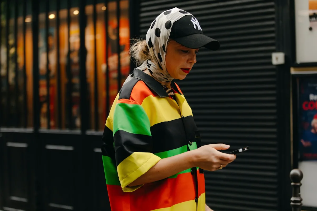 Kobieta w barwnym stroju używa smartfona podczas spaceru po mieście. Zdjęcie oddaje powszechność urządzeń mobilnych i rosnące znaczenie bezpieczeństwa danych w życiu codziennym.