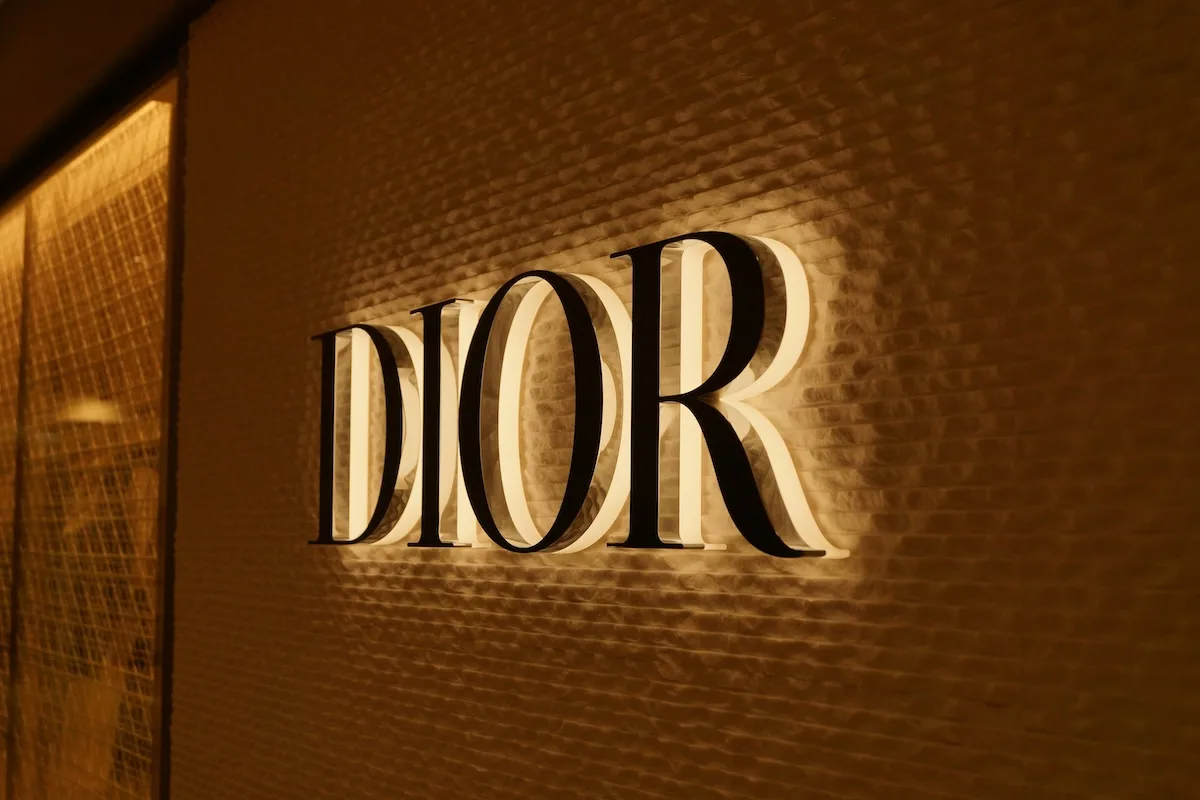 Oświetlone logo Dior na eleganckiej ścianie we wnętrzu ekskluzywnego butiku. Marka przynależy do grupy LVMH i stanowi element segmentu mody, który odnotował redukcję sprzedaży w pierwszym kwartale 2026 roku.