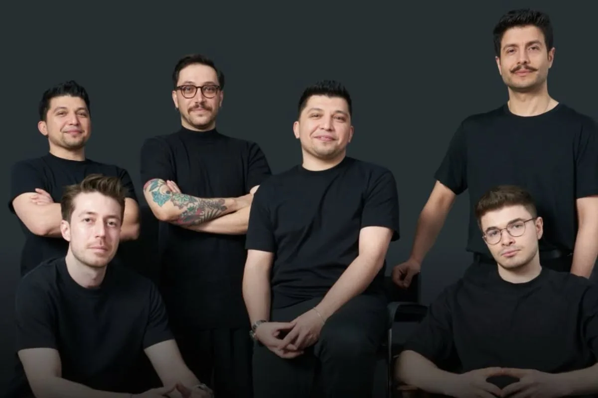 Replenit AI retail. Grupa sześciu panów w czarnych T-shirtach pozuje do zdjęcia na neutralnym, stonowanym tle – niektórzy stoją, inni siedzą, spoglądając w kamerę.