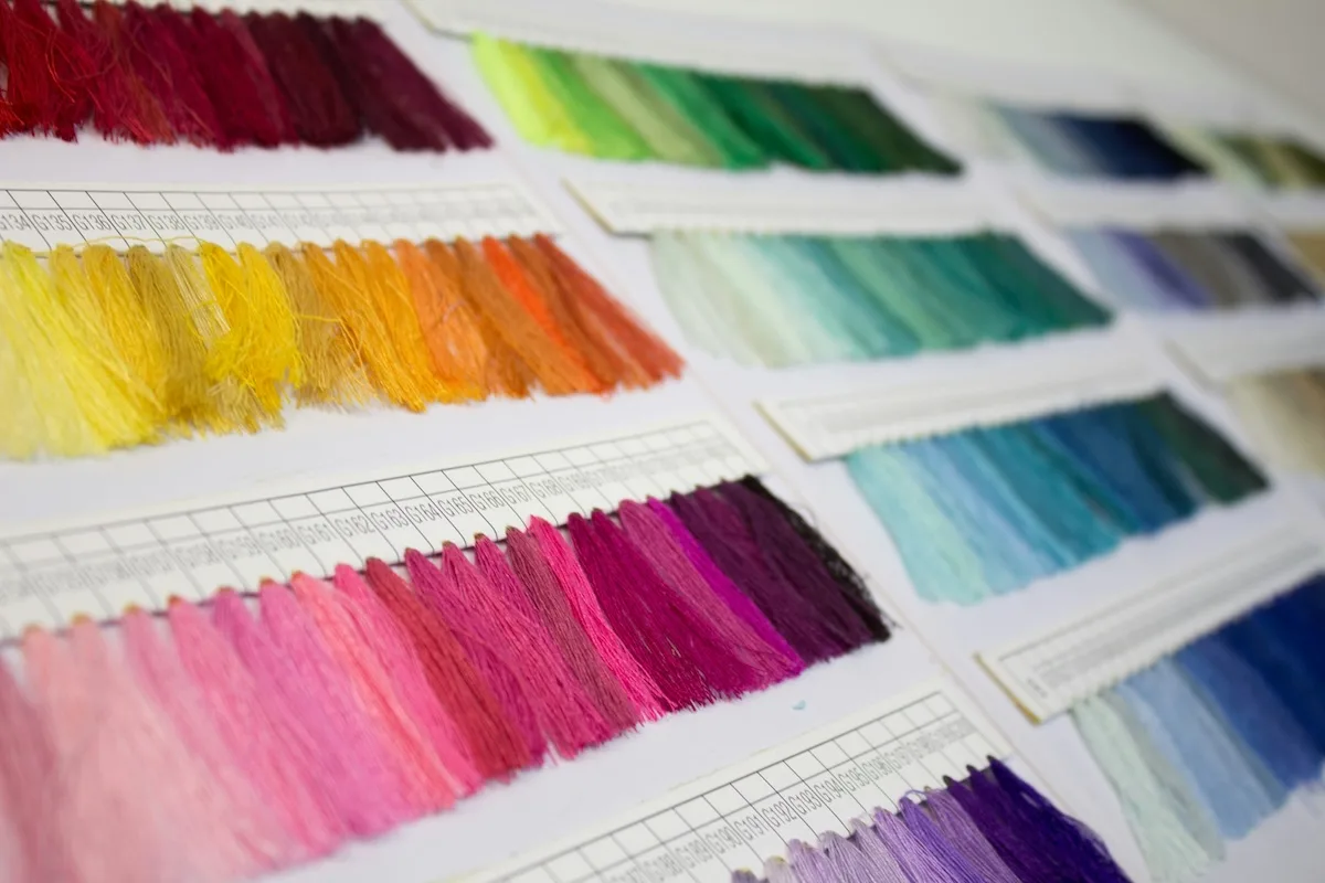 Próbki kolorowych nici ułożone w paletach pokazujące różnorodność barw stosowanych w produkcji tekstyliów. Zdjęcie ilustruje etap projektowania i przygotowania materiałów w branży odzieżowej.