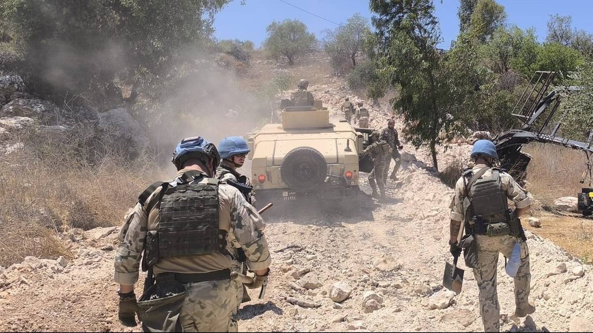 Polscy żołnierze w mundurach i hełmach z niebieskimi oznaczeniami ONZ idą po kamienistej drodze w kierunku pojazdu wojskowego.