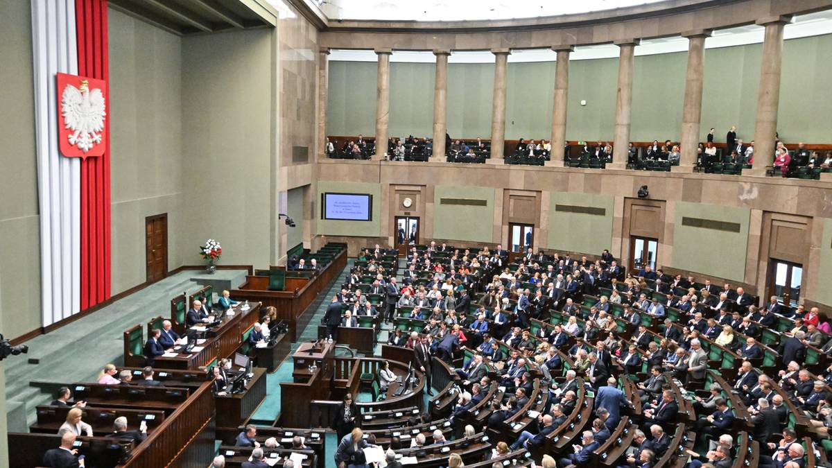 Sala plenarna Sejmu RP z posłami zasiadającymi w ławach i polską flagą z godłem.