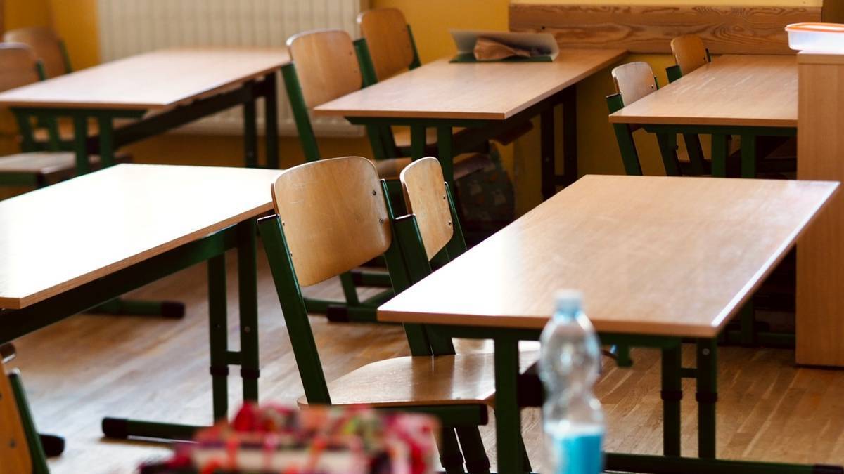 Zdjęcie przedstawia puste sale lekcyjne w szkole, z rzędami drewnianych ławek i krzeseł.