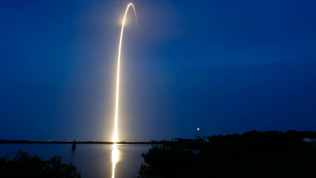 Jasny tor światła z rakiety wznoszącej się na nocnym niebie nad wodą.