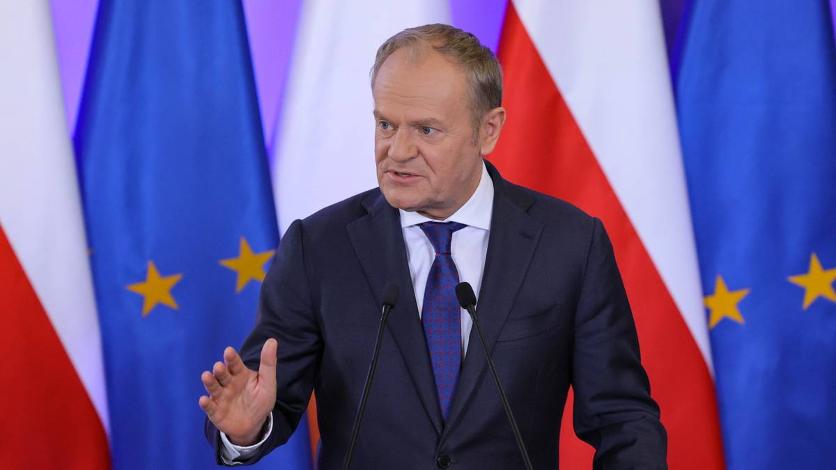 Donald Tusk przemawia na tle flag Polski i Unii Europejskiej.