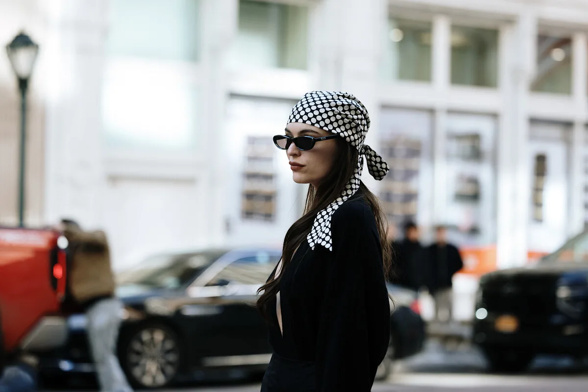 Rynek dóbr luksusowych Bliski Wschód. Elegancko odziana kobieta w stylizacji premium na tle scenerii miejskiej obrazuje światowego klienta towarów luksusowych, którego wybory zakupowe w znacznym stopniu zależą od stabilności i nastrojów. W obliczu napięć na Bliskim Wschodzie tacy właśnie konsumenci częściej wstrzymują się z zakupami lub przekierowują wydatki, mając wpływ na cały rynek.