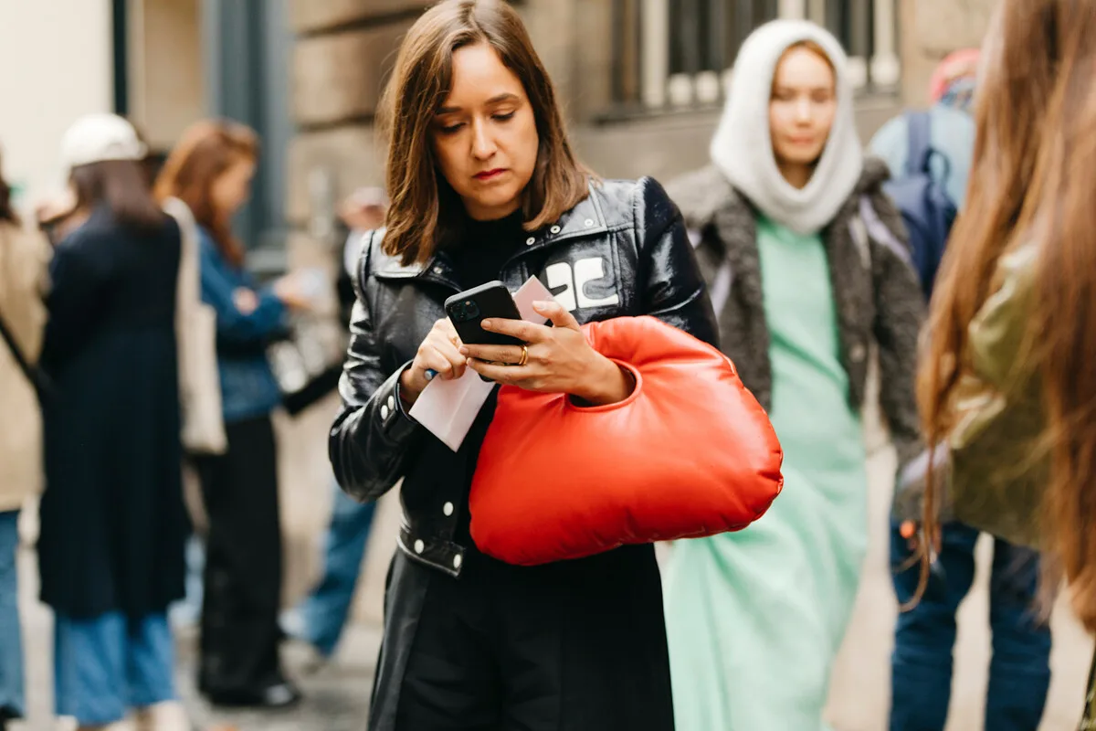 Wyciek danych z Alibaba. Kobieta z czerwoną torbą spogląda w smartfon na zatłoczonej ulicy. Scena odnosi się do kwestii ochrony danych i tego, jak często dzielimy się informacjami w przestrzeni wirtualnej.
