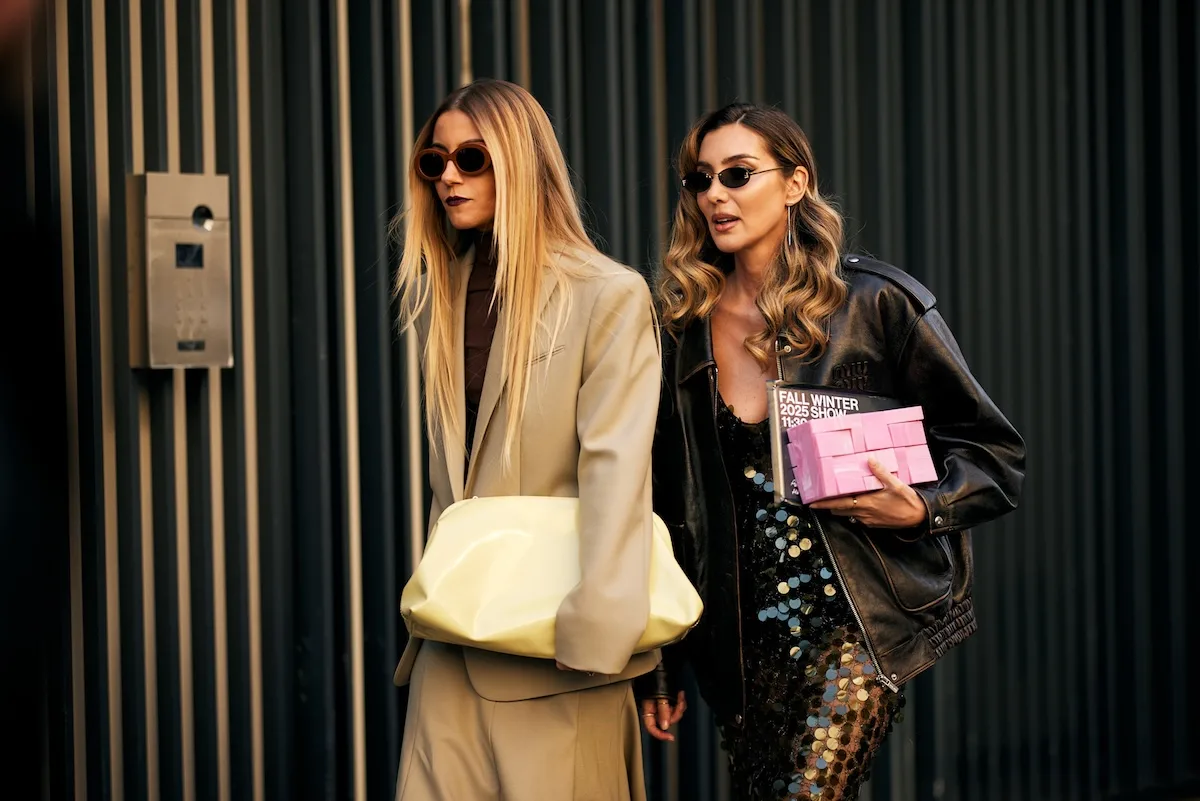 Wielki Czwartek, do której sklepy są otwarte w 2026 roku? Dwie elegancko ubrane panie w ciemnych okularach opuszczają budynek, jedna trzyma pokaźną, jasną torbę, druga karton z napisem „Pokaz Jesień Zima 2025”.