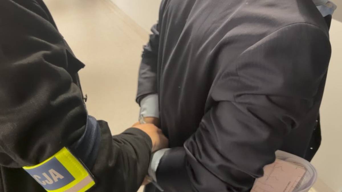 Policjant zakłada kajdanki zatrzymanemu mężczyźnie.