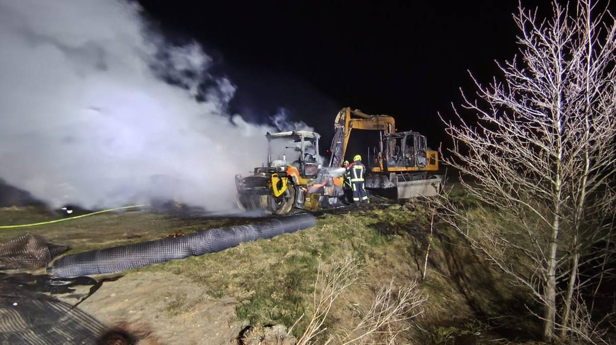 Płonące maszyny budowlane na placu budowy, w tle unoszą się kłęby dymu.