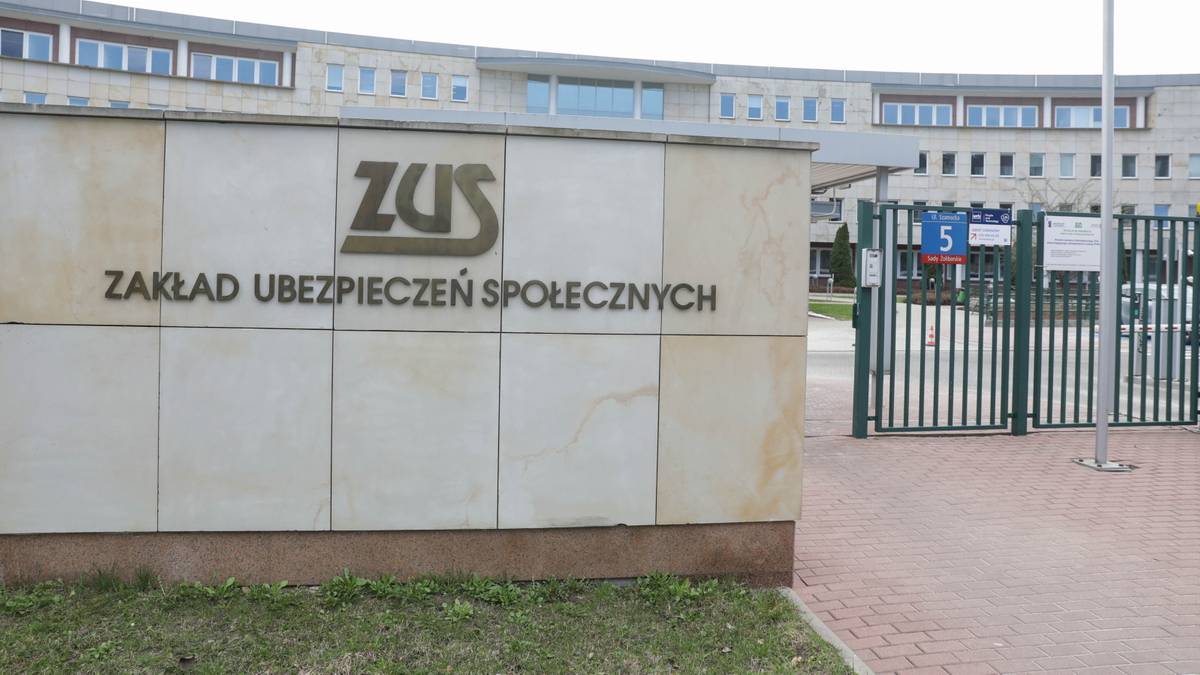 Naprzeciwko kamiennej ściany z napisem ZUS ZAKŁAD UBEZPIECZEŃ SPOŁECZNYCH znajduje się brama wjazdowa na teren plac&oacute;wki.