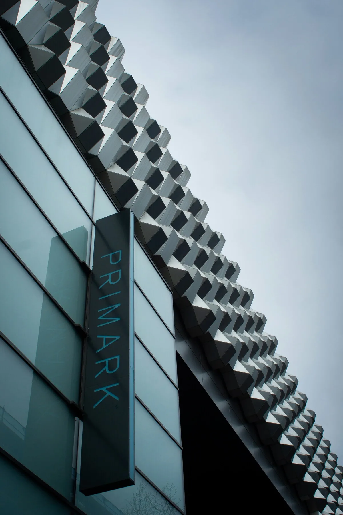 Nowoczesna elewacja sklepu Primark z charakterystycznym geometrycznym motywem na fasadzie. Na budynku widnieje pionowe logo marki, a całość utrzymana jest w minimalistycznej, miejskiej stylistyce.