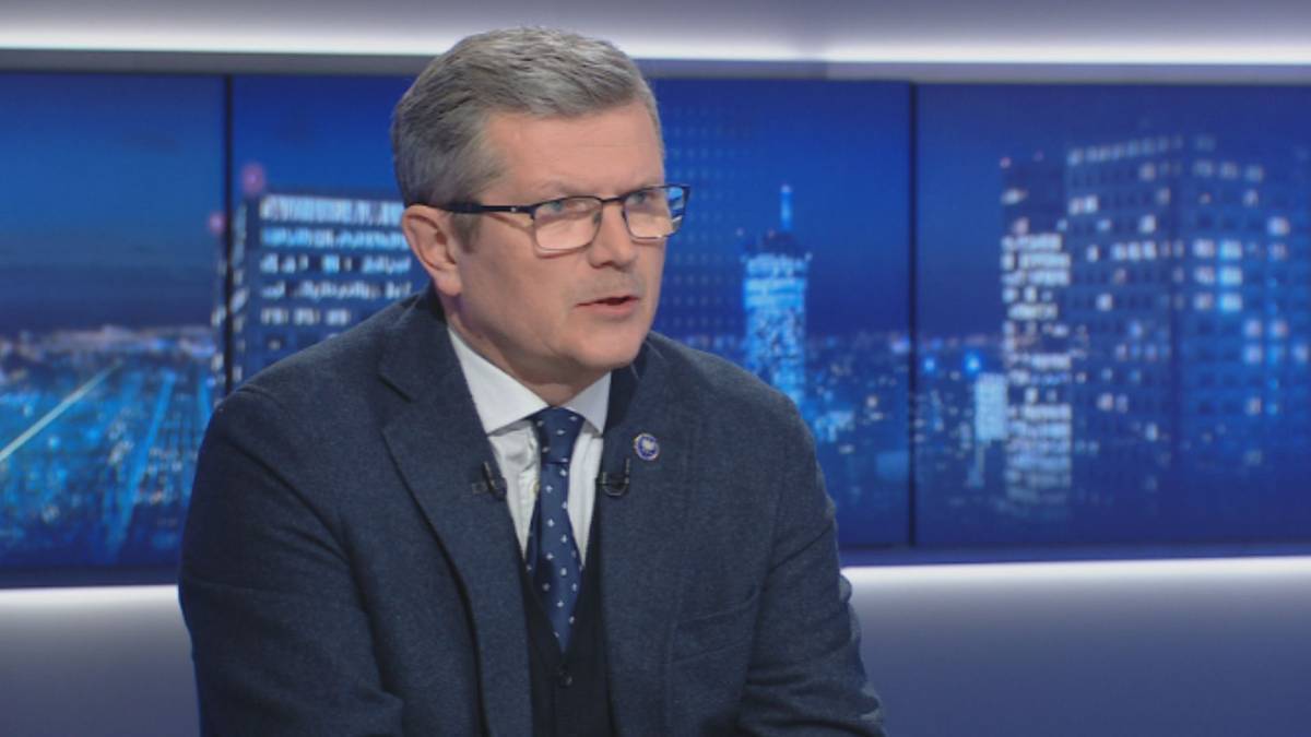 Mężczyzna w garniturze i okularach siedzi w studiu telewizyjnym, patrząc w bok i m&oacute;wiąc.