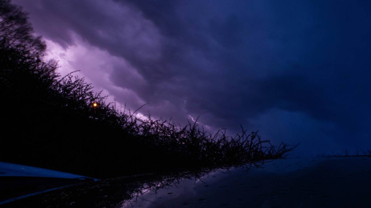 Mroczne chmury burzowe z przebłyskami błyskawic nad ciemnym, wodnistym krajobrazem.