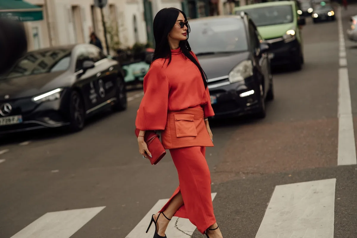 Elegancka kobieta w czerwonej stylizacji przechodząca przez ulicę w miejskiej przestrzeni, na tle samochodów i zabudowy miejskiej