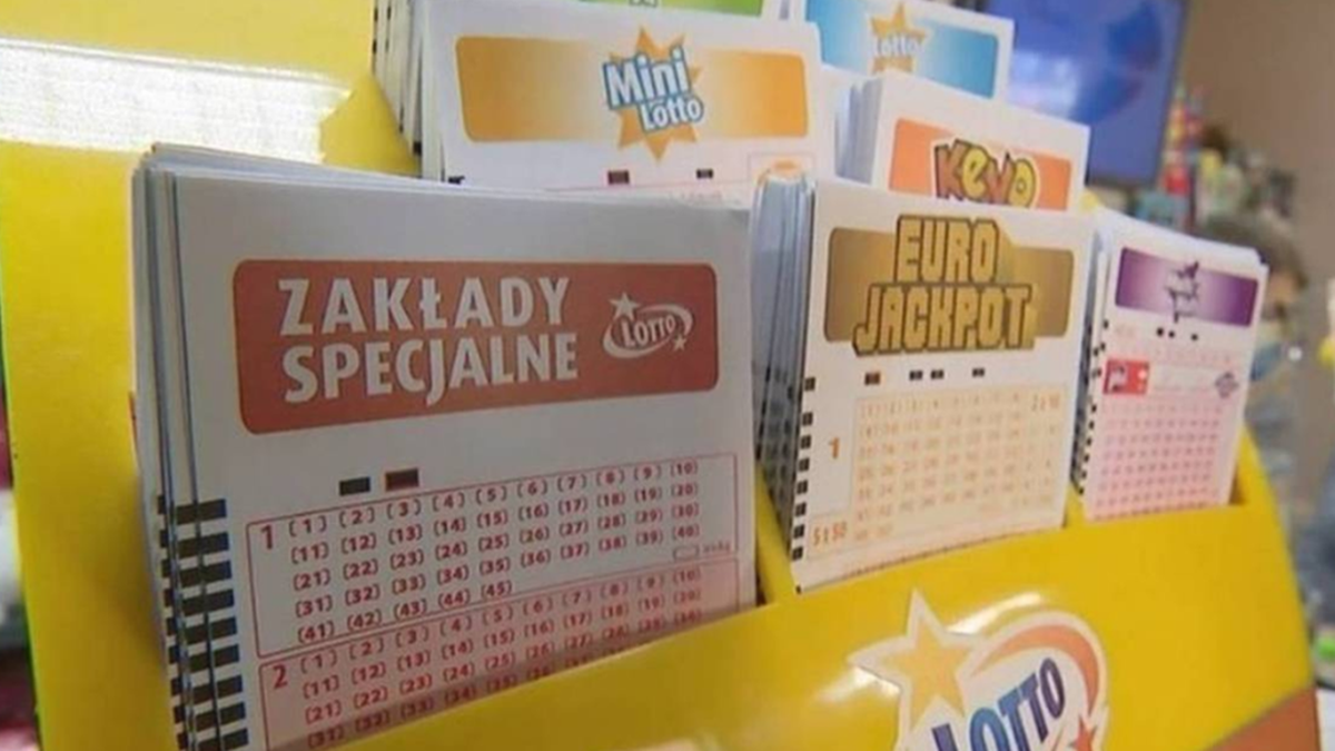 Stos kupon&oacute;w gier liczbowych Lotto, w tym zakład&oacute;w specjalnych, Mini Lotto i Euro Jackpot, umieszczony w ż&oacute;łtym stojaku.