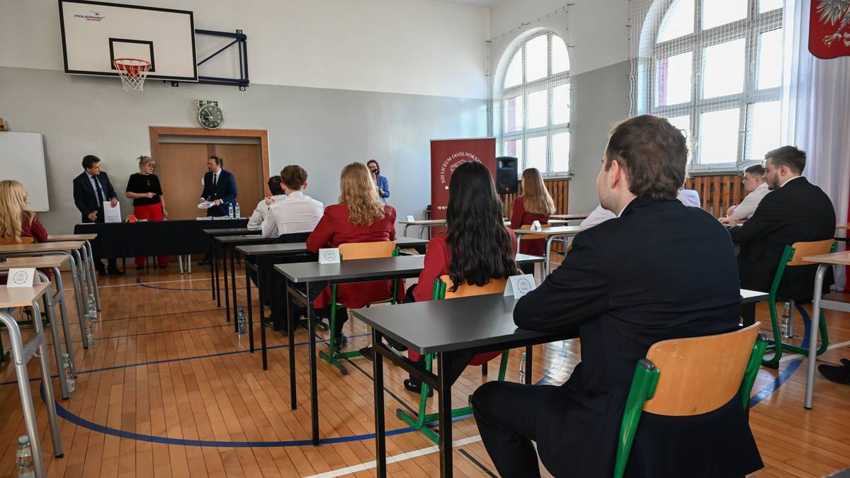 Uczniowie siedzą przy ławkach w sali egzaminacyjnej, podczas pisania egzaminu maturalnego.