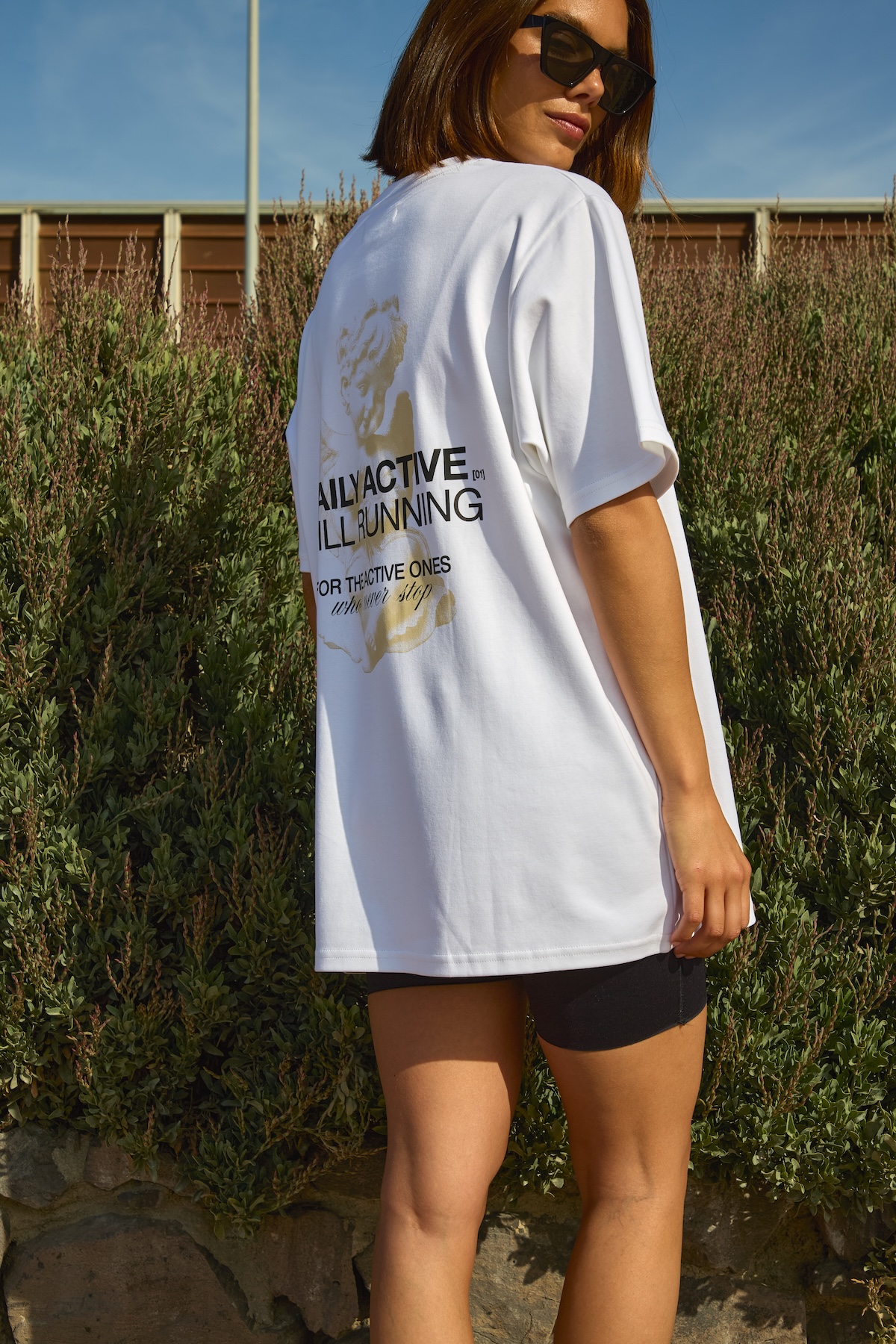 Biały oversize T-shirt MISAGA Daily Active Still Running zestawiony z kolarkami i okularami przeciwsłonecznymi.