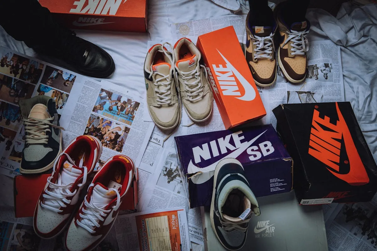 Nike pozew klientów. Na zdjęciu: kolekcja butów Nike ułożona obok charakterystycznych pudełek z logo marki. Na zdjęciu widać różne modele obuwia sportowego i sneakersów rozmieszczone na tle gazet i materiałów promocyjnych.