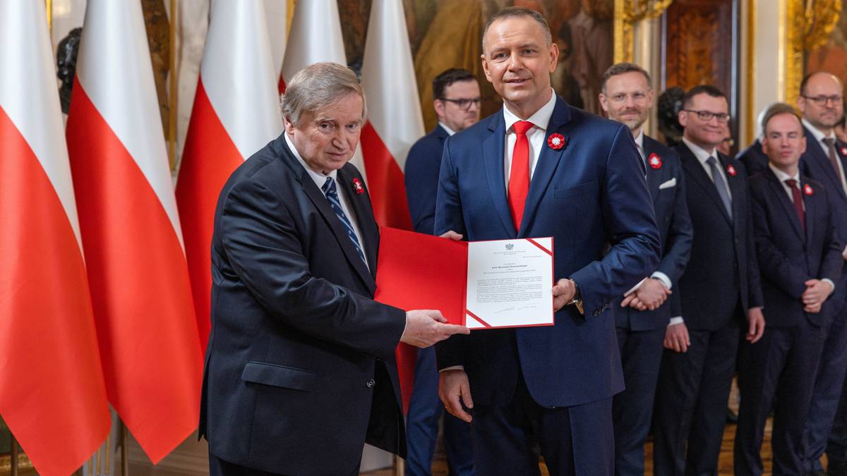 Dw&oacute;ch mężczyzn w garniturach odbiera dokumenty na tle flag Polski.