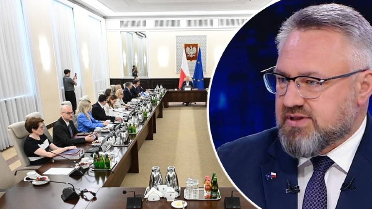 Fragment twarzy mężczyzny w okularach na pierwszym planie, w tle sala konferencyjna z ludźmi siedzącymi przy długim stole.