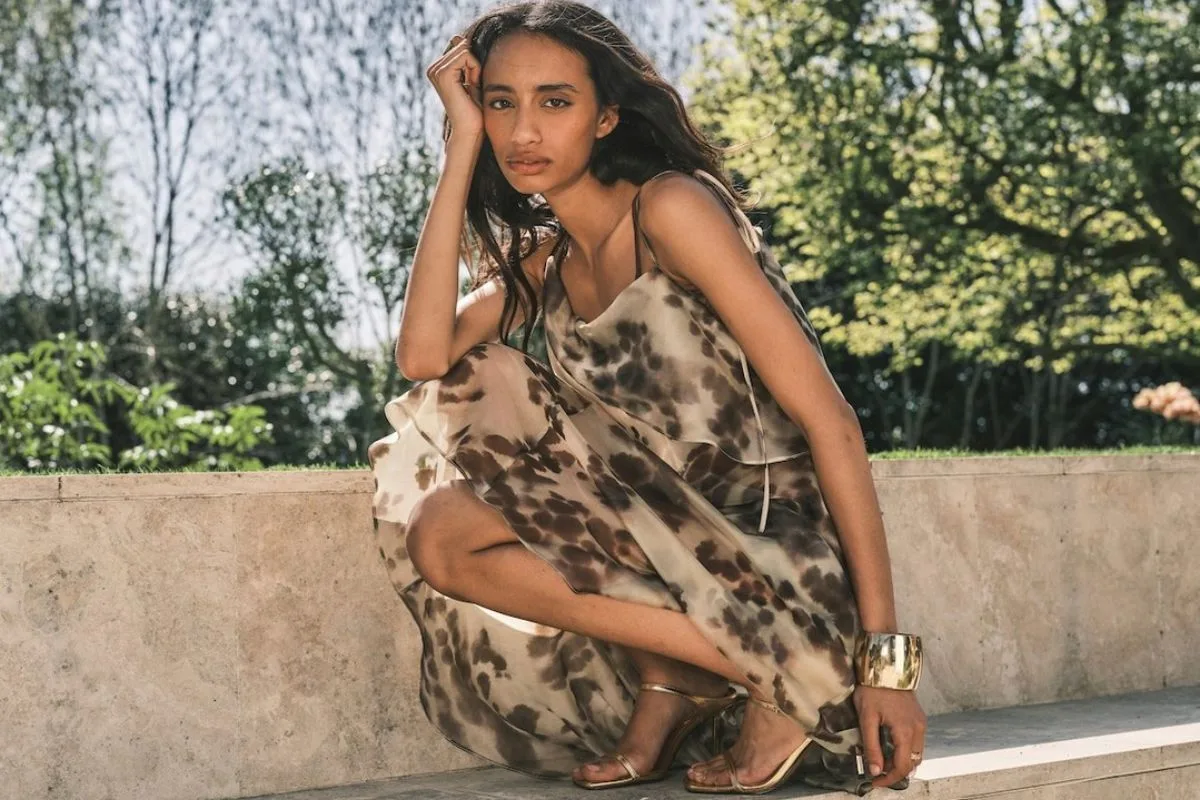Topshop sklepy stacjonarne. Modelka w zwiewnej sukience midi i sandałach na obcasie prezentuje nowoczesny styl inspirowany estetyką luksusowych marek. Trendy tego typu przez lata były ważną częścią oferty Topshopu i brytyjskiej mody high street.
