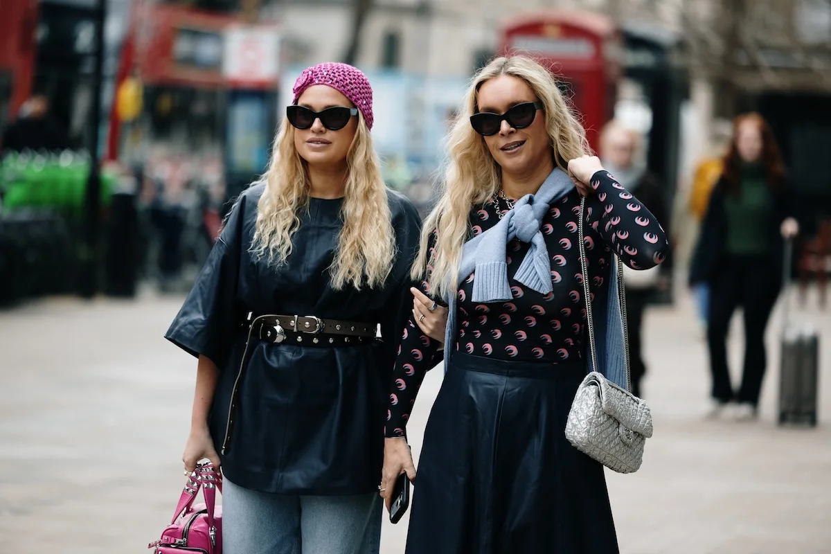 Program rekomendacji Vinted. Dwie kobiety w kreacjach street style przechadzają się po mieście, prezentując odzież z drugiej ręki i codzienny wygląd inspirowany trendami resale. Zdjęcie odnosi się do wzrastającej popularności platform takich jak Vinted oraz aktywności użytkowników, którzy sprzedają i nabywają odzież online. Tego rodzaju stylizacje często pojawiają się w ofertach aplikacji second hand, wspierając rozwój programów rekomendacji i społeczności.
