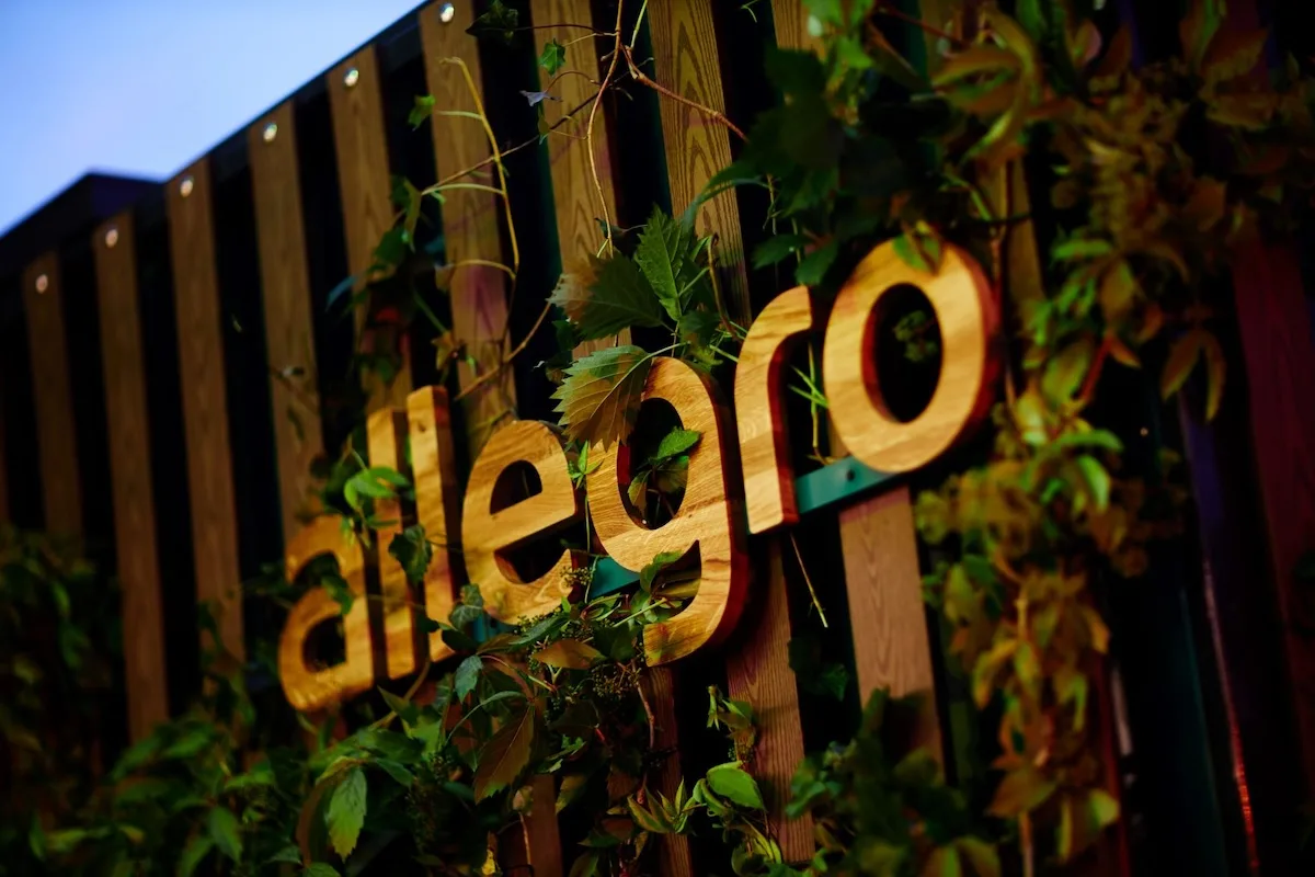Logo Allegro otoczone zielenią podczas wydarzenia marki. Allegro rozwija nowoczesne technologie AI i wdraża Inteligentnego Asystenta w aplikacji mobilnej, przeobrażając sposób dokonywania zakupów online.